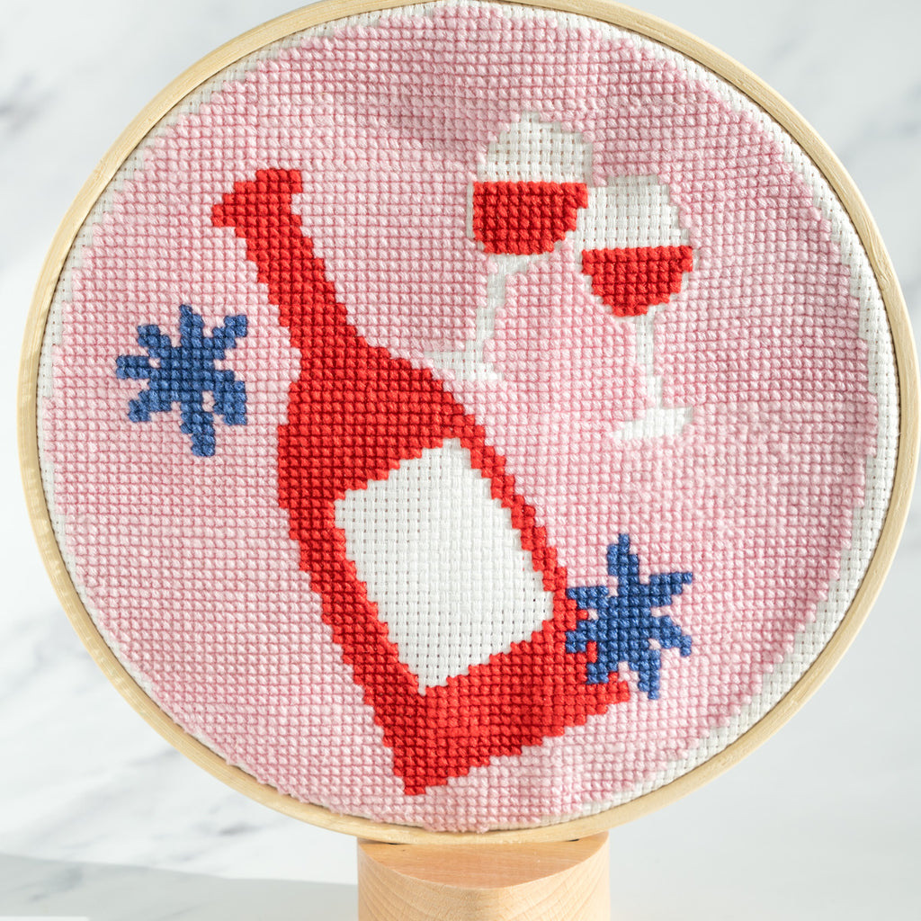 Wine bottle and glasses completed cross stitch piece on grey background 