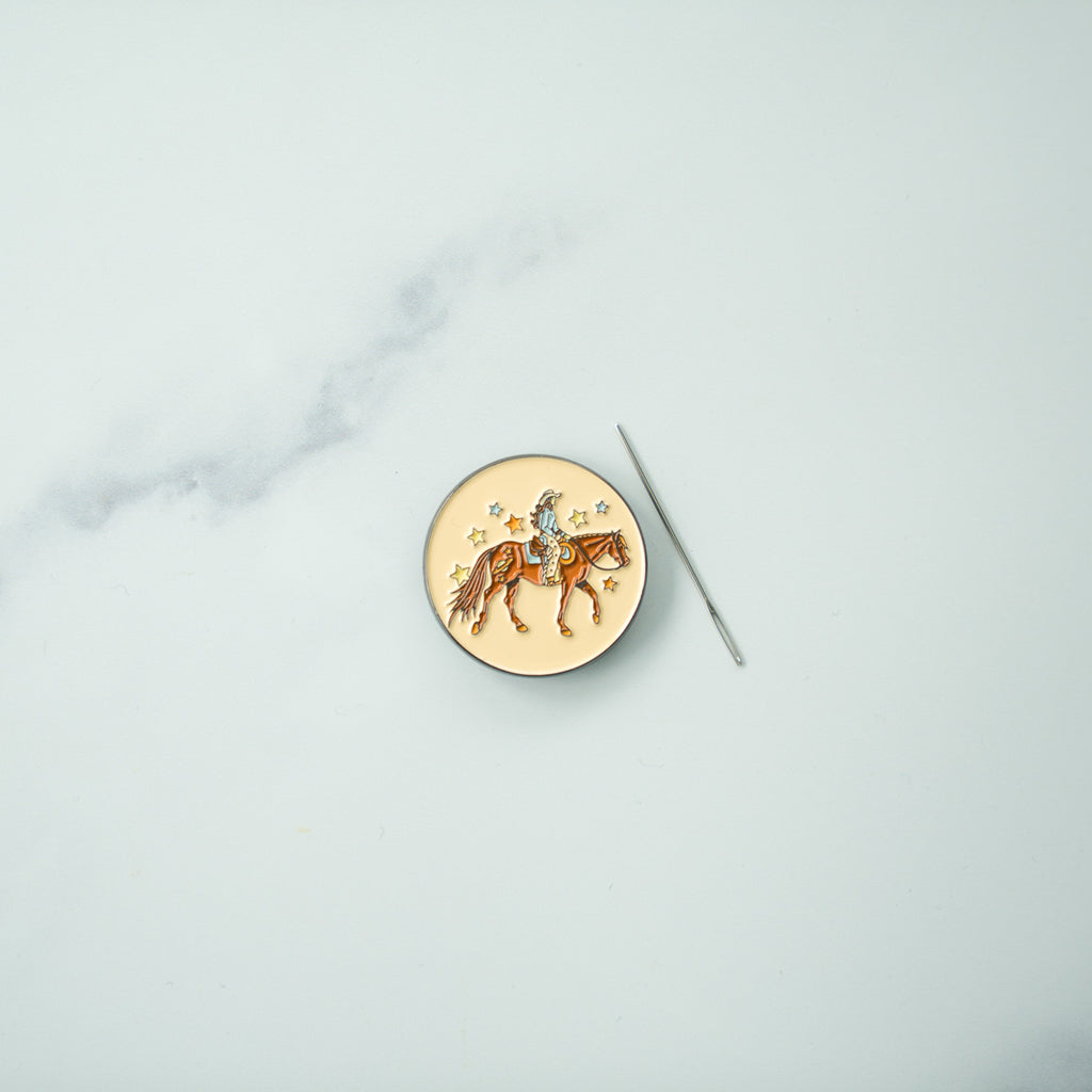 Cowgirl on horse surrounded by stars on peach enamel needle minder 